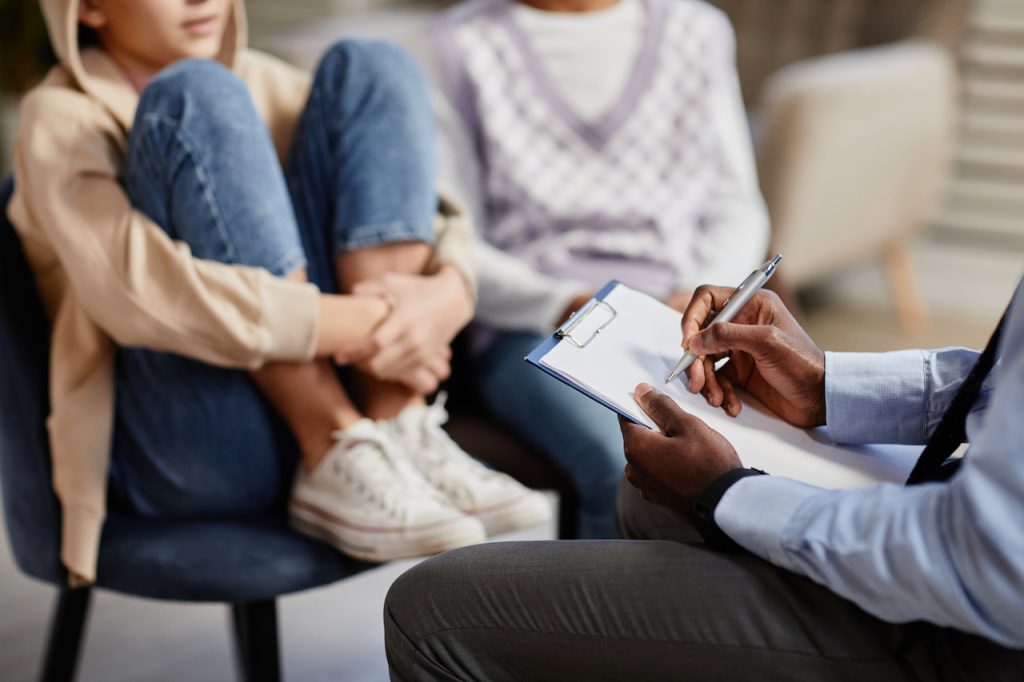 Primer plano de un psicólogo afroamericano tomando notas en un portapapeles en una sesión de terapia para niños.