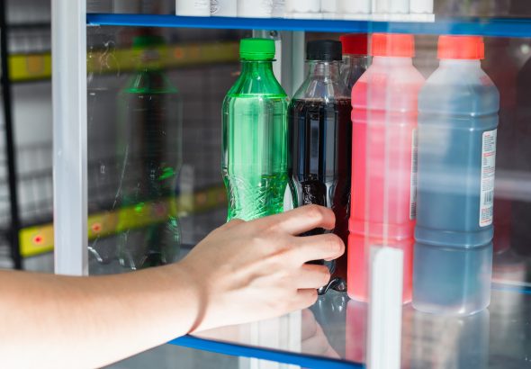 Mano de una chica que sostiene un refresco azucarado, sacándolo de una vitrina de cristal en una tienda