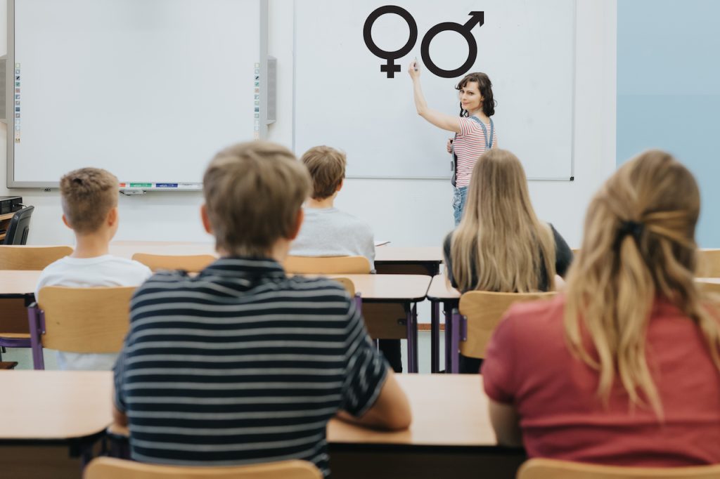 Joven profesora está de pie delante de la pizarra durante la lección de educación sexual