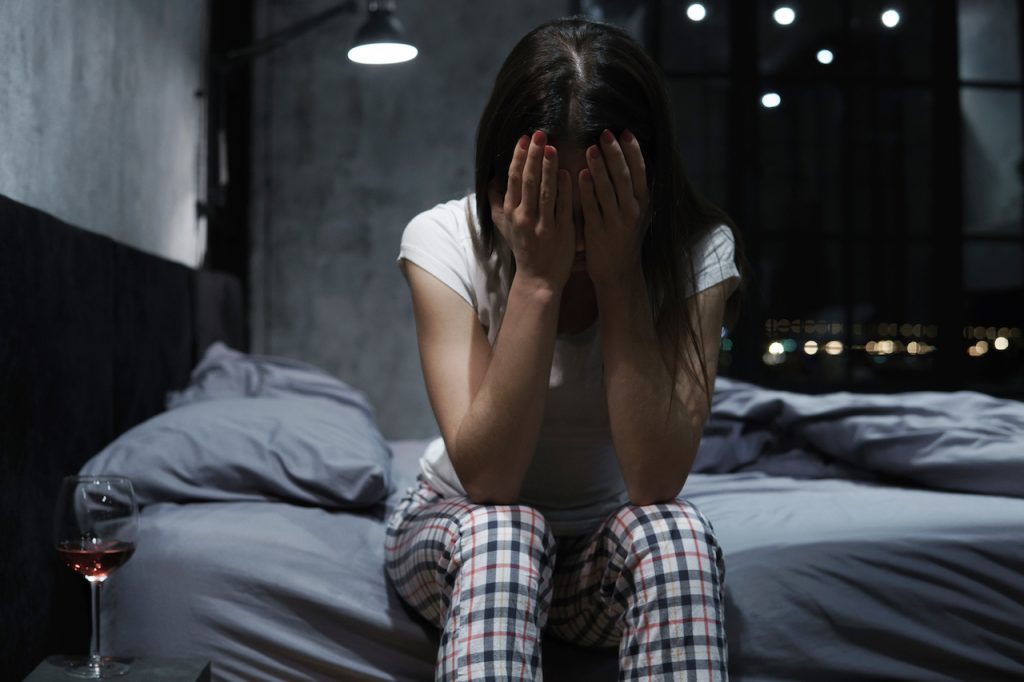 Mujer joven que se cubre la cara con las manos, pasa la noche en vela, se siente desamparada y llora.