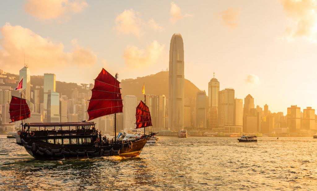 Barco chino de velas rojas de madera en el puerto Victoria de Hong Kong al atardecer