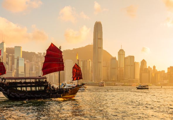 Barco chino de velas rojas de madera en el puerto Victoria de Hong Kong al atardecer